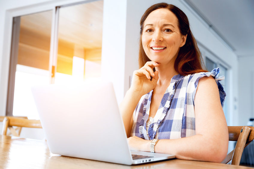 Mature beautiful woman sitting at the table and working on her laptop