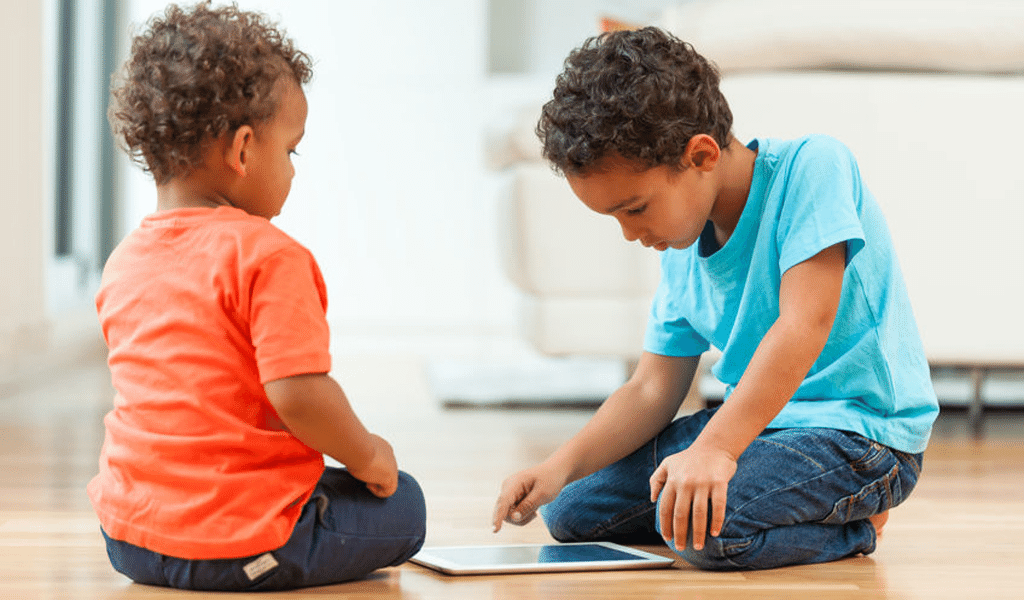 two boys playing with tablet on the floor