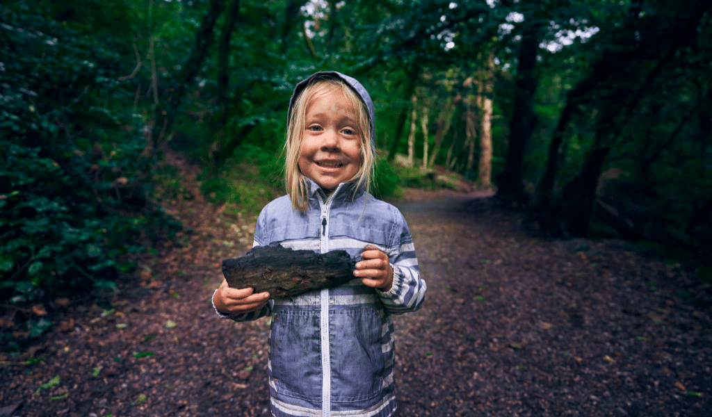 child holding a piece of wood in a forest