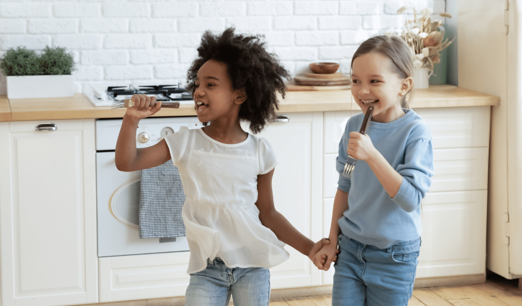 black girl and white girl singing in kitchen using kitchen utensils