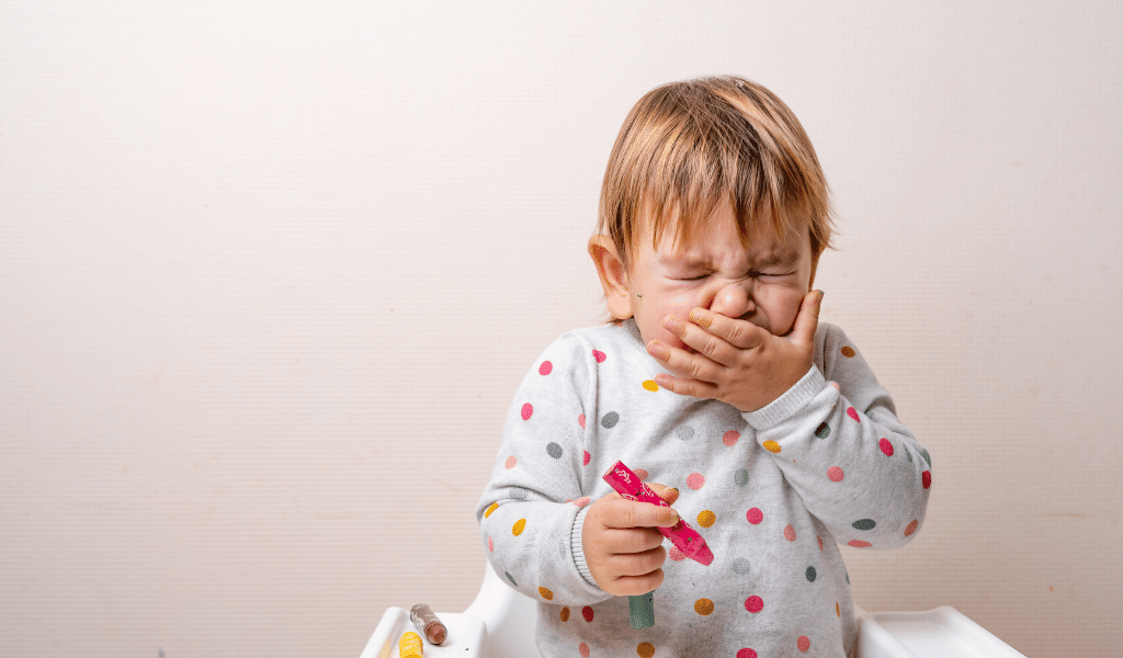 child aged 2 covering his face with one hand while he sneezes