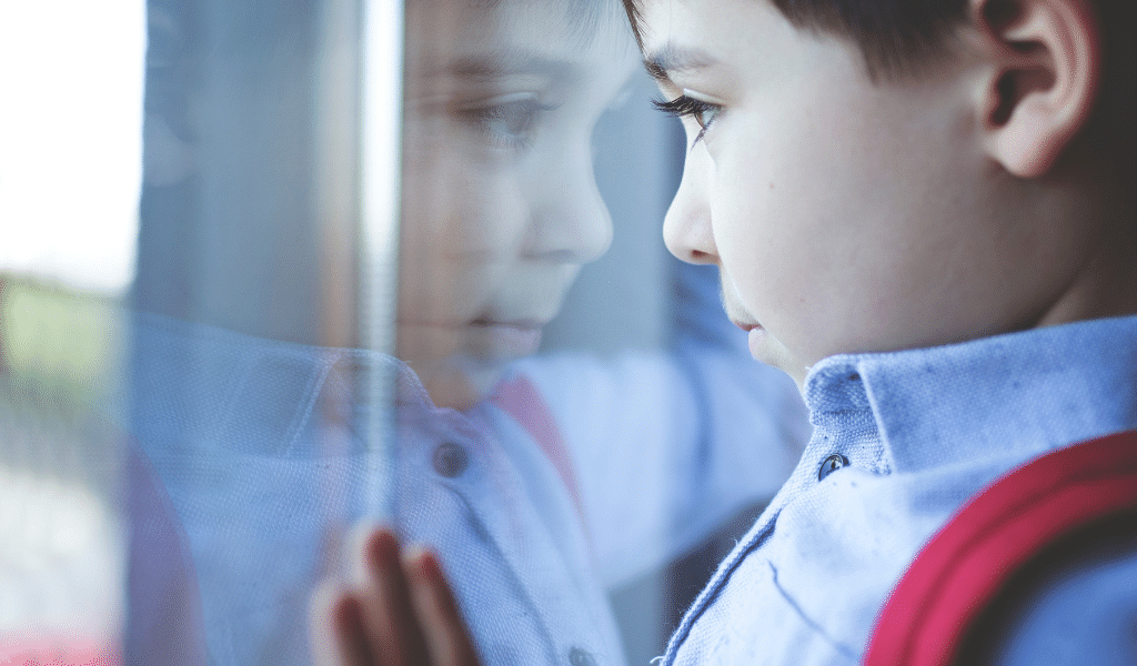 child looking through a glass door pensive