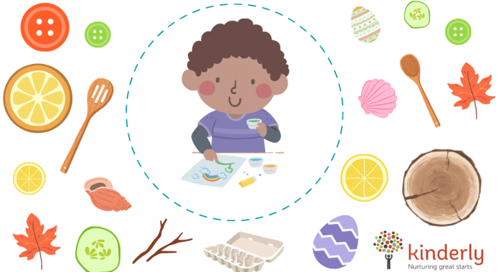 Black child painting surrounded by loose parts including buttons, leaves, wooden spoons, eggs or fruit slices