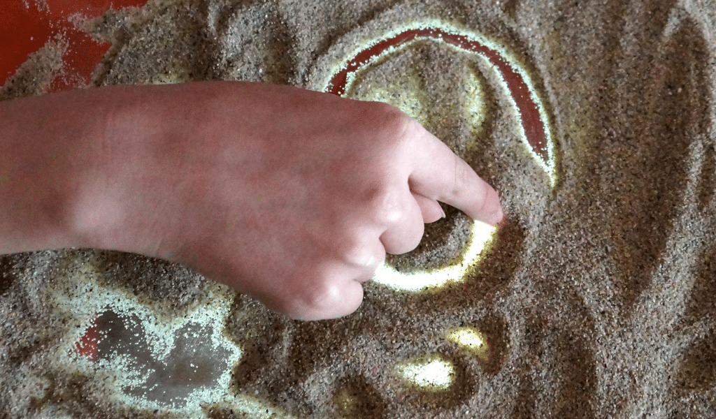 child's hand making marks with sand
