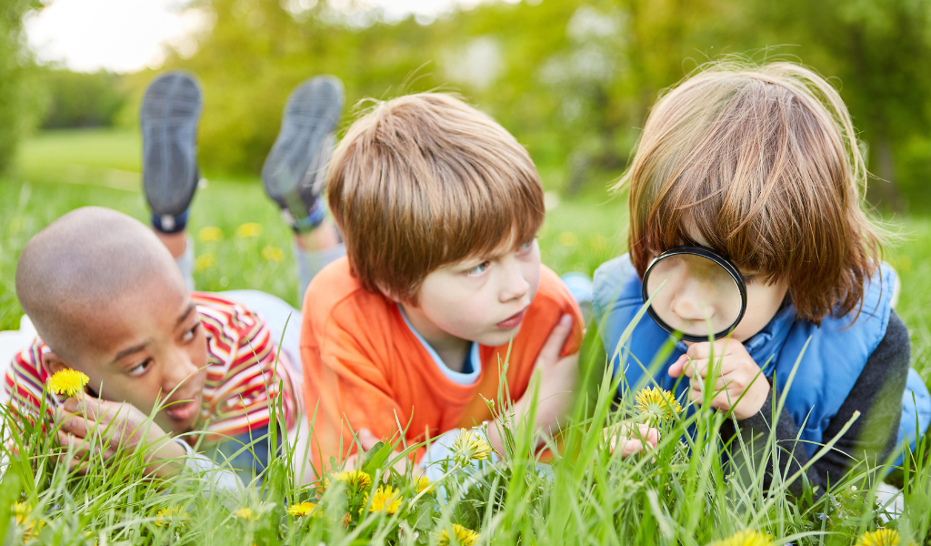 children with magnifying glass playin in grass